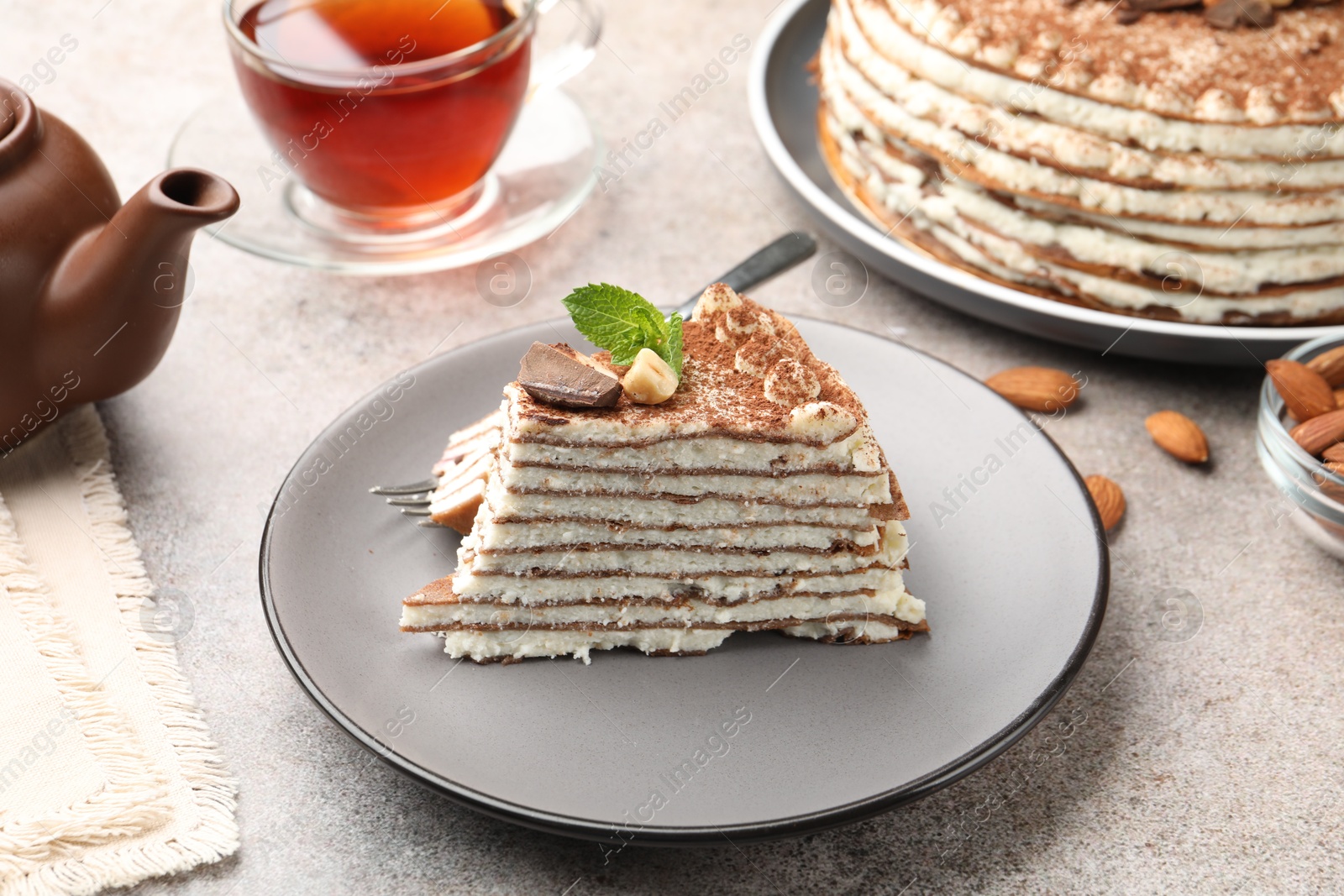 Photo of Piece of tasty crepe cake with cocoa powder, chocolate and nuts served on light table, closeup