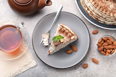 Photo of Piece of tasty crepe cake with cocoa powder, chocolate and nuts served on light table, flat lay