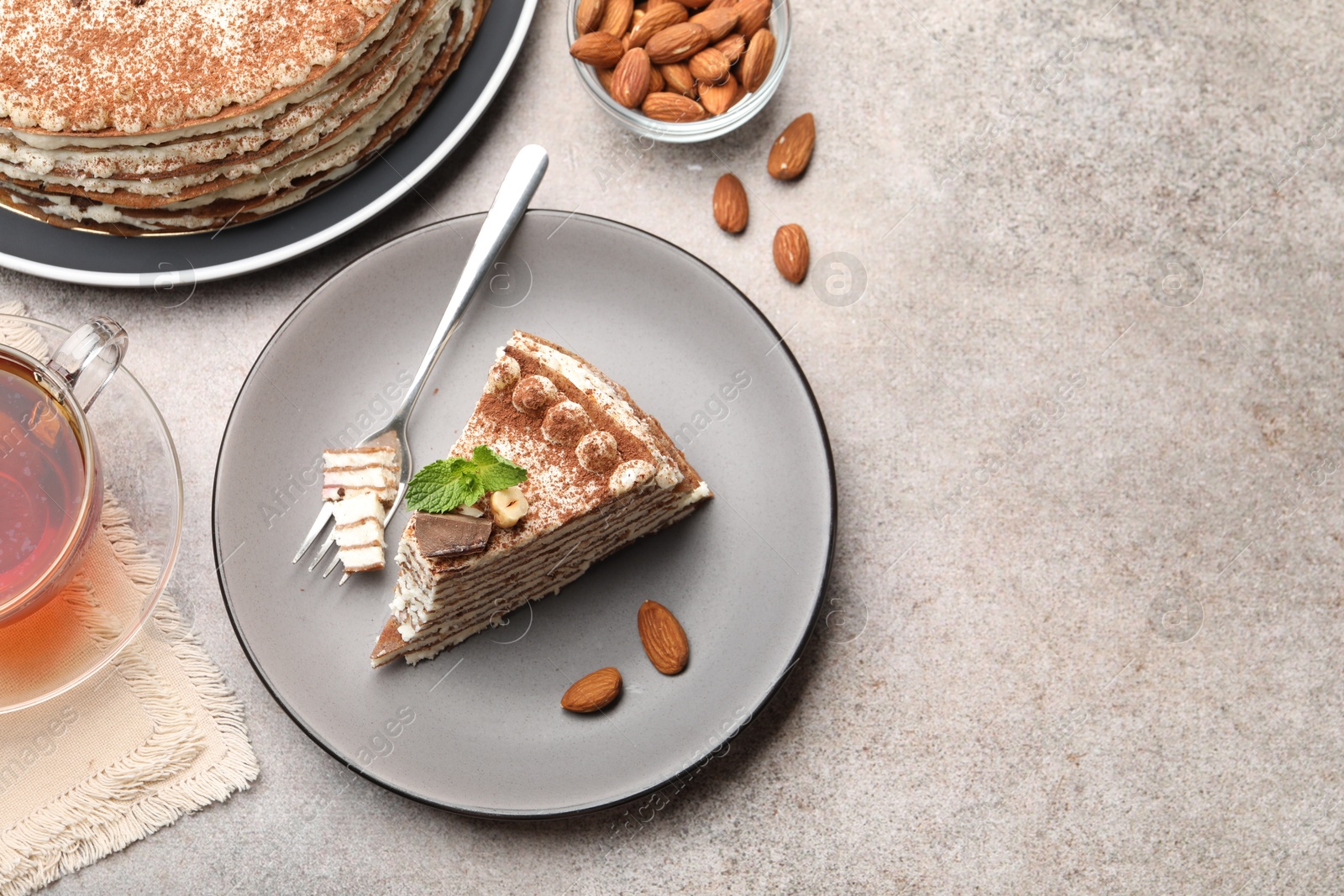 Photo of Piece of tasty crepe cake with cocoa powder, chocolate and nuts served on light table, flat lay. Space for text