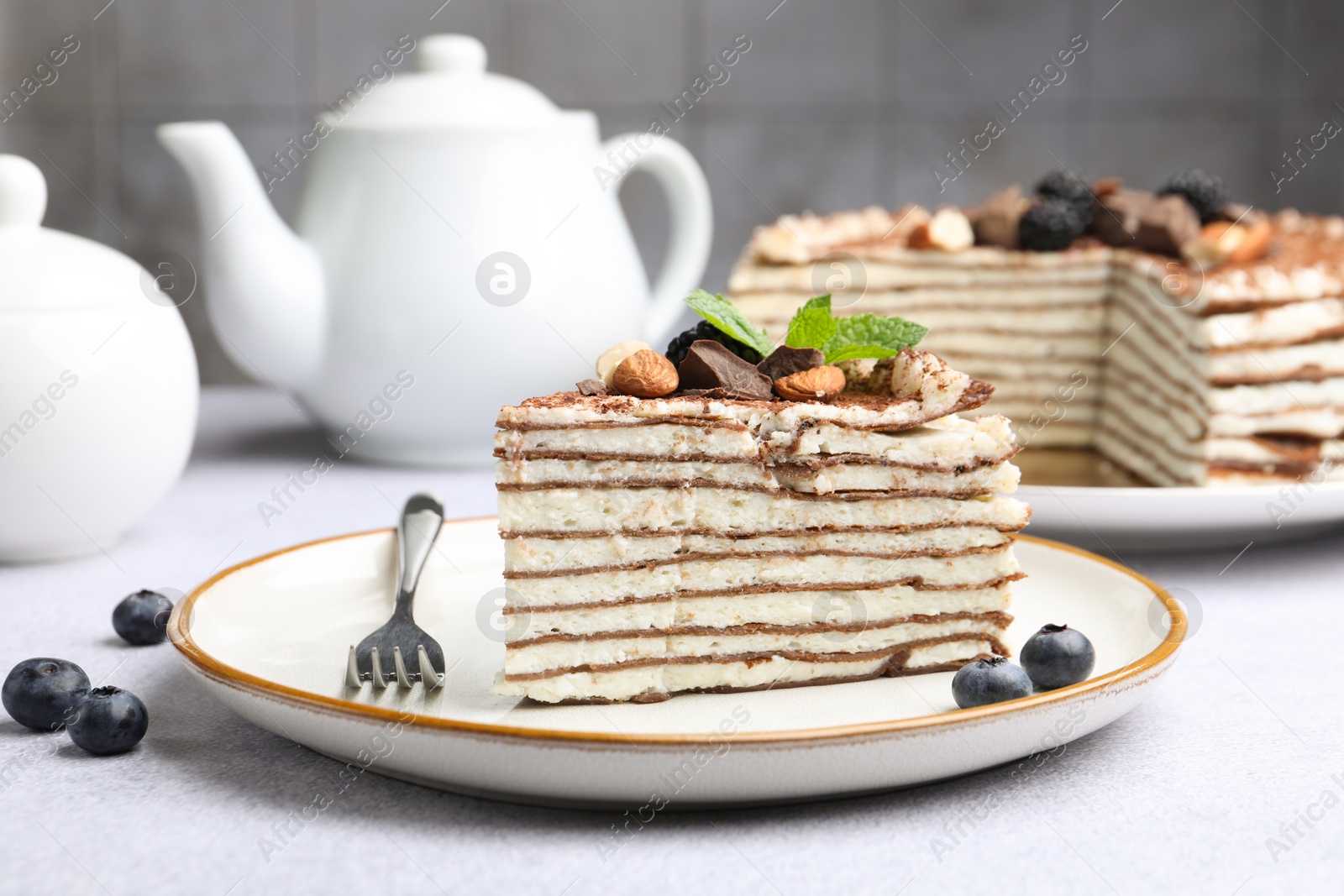 Photo of Piece of tasty crepe cake with cocoa powder, chocolate, nuts and blackberry served on light table, closeup