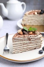 Photo of Piece of tasty crepe cake with cocoa powder, chocolate, nuts and blackberry served on light table, closeup