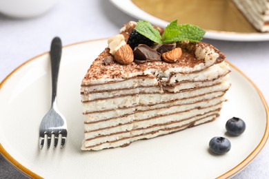 Photo of Piece of tasty crepe cake with cocoa powder, chocolate, nuts and blackberry served on light table, closeup