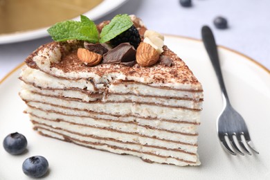 Photo of Piece of tasty crepe cake with cocoa powder, chocolate, nuts and blackberry served on light table, closeup