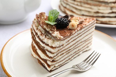 Photo of Piece of tasty crepe cake with cocoa powder, chocolate, nuts and blackberry served on light table, closeup