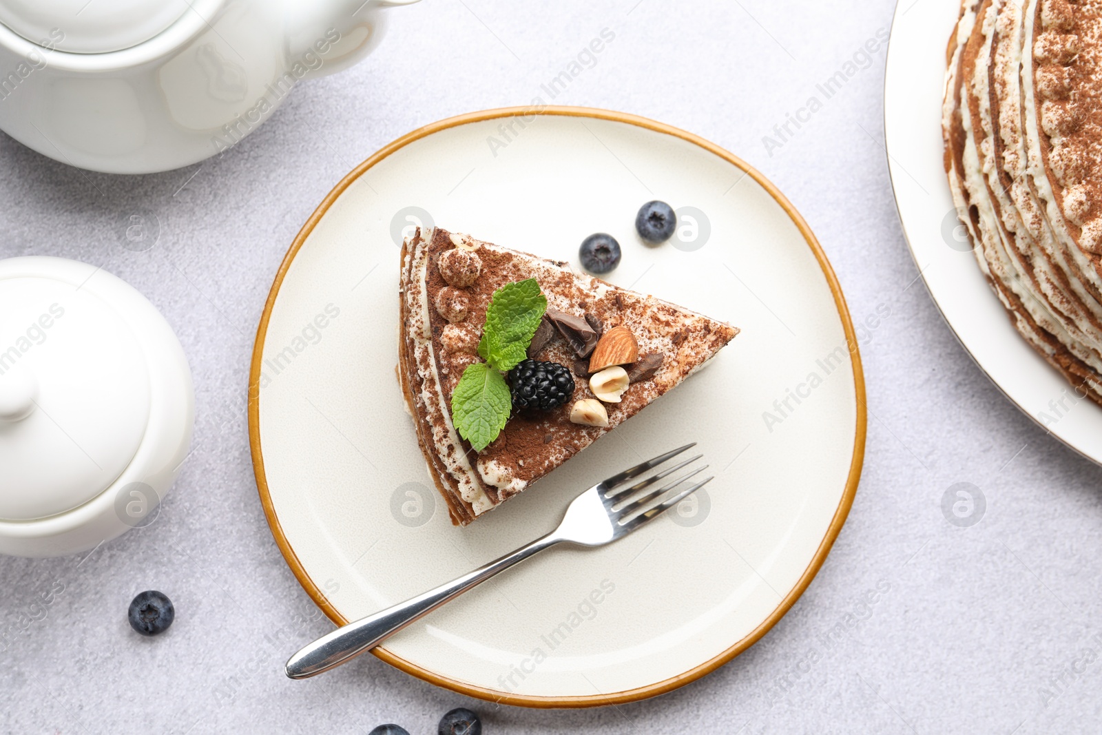Photo of Piece of tasty crepe cake with cocoa powder, chocolate, nuts and blackberry served on light table, flat lay
