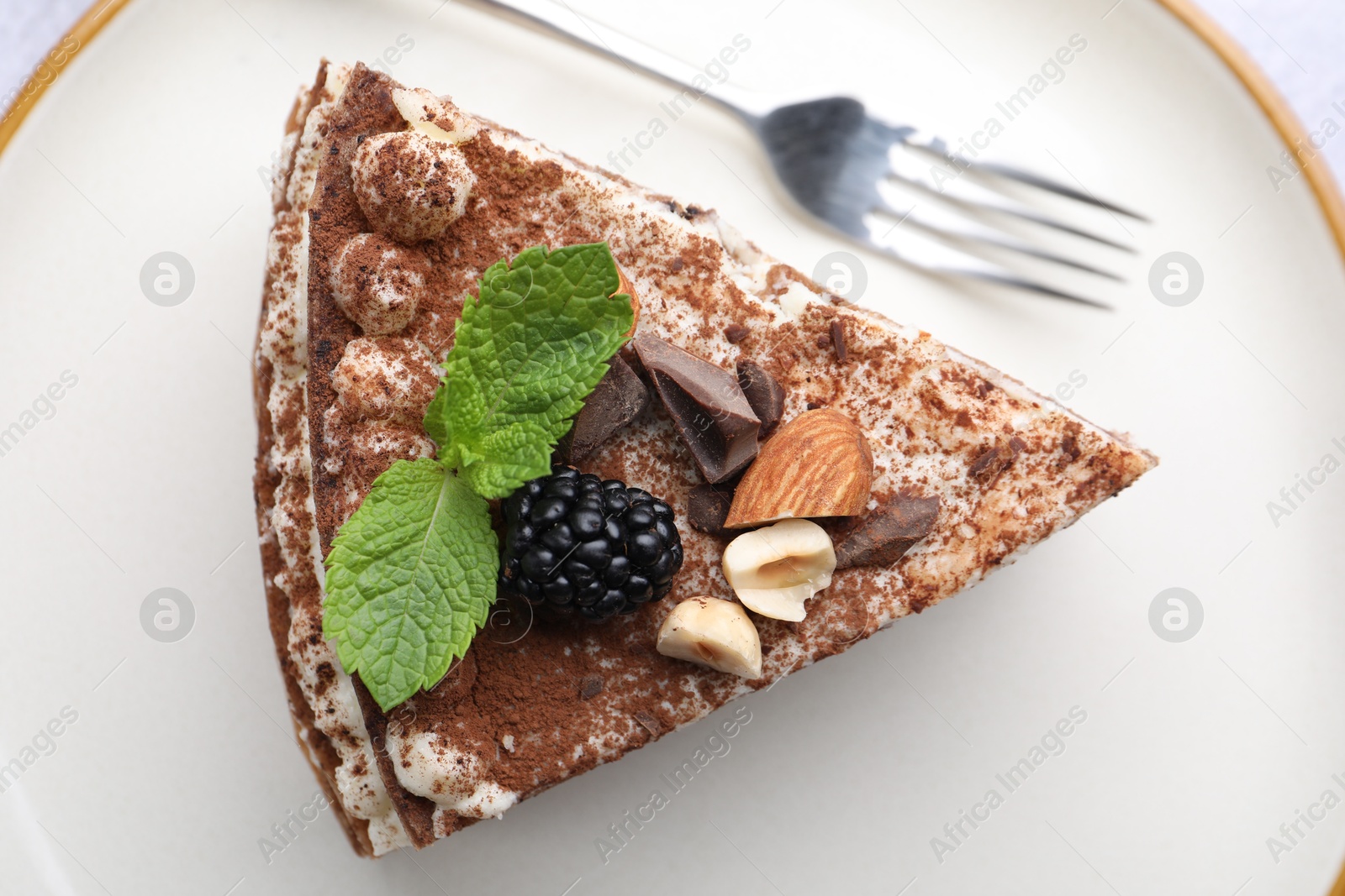 Photo of Piece of tasty crepe cake with cocoa powder, chocolate, nuts and blackberry served on table, top view