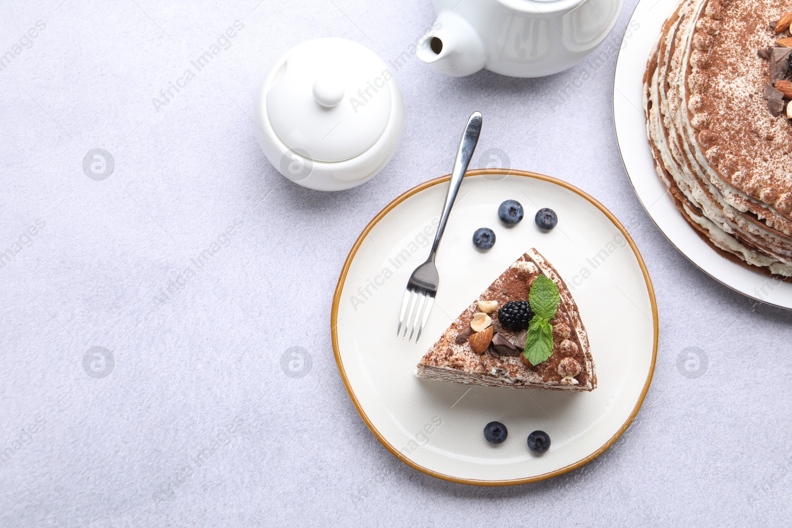 Photo of Piece of tasty crepe cake with cocoa powder, chocolate, nuts and blackberry served on light table, flat lay. Space for text