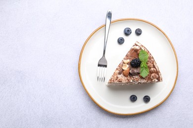 Photo of Piece of tasty crepe cake with cocoa powder, chocolate, nuts and blackberry served on light table, top view. Space for text