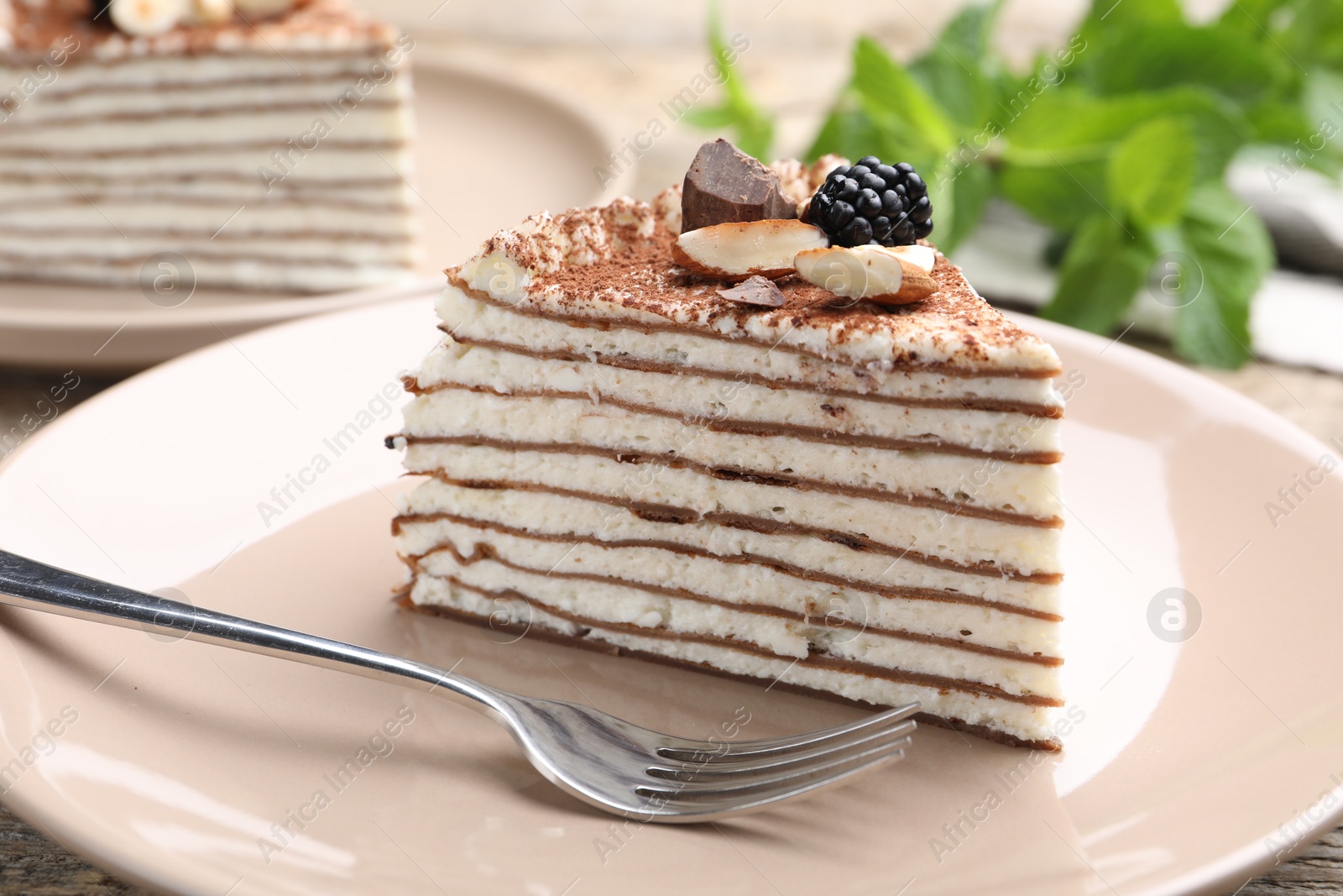 Photo of Piece of tasty crepe cake with cocoa powder, chocolate, nuts and blackberry served on wooden table, closeup