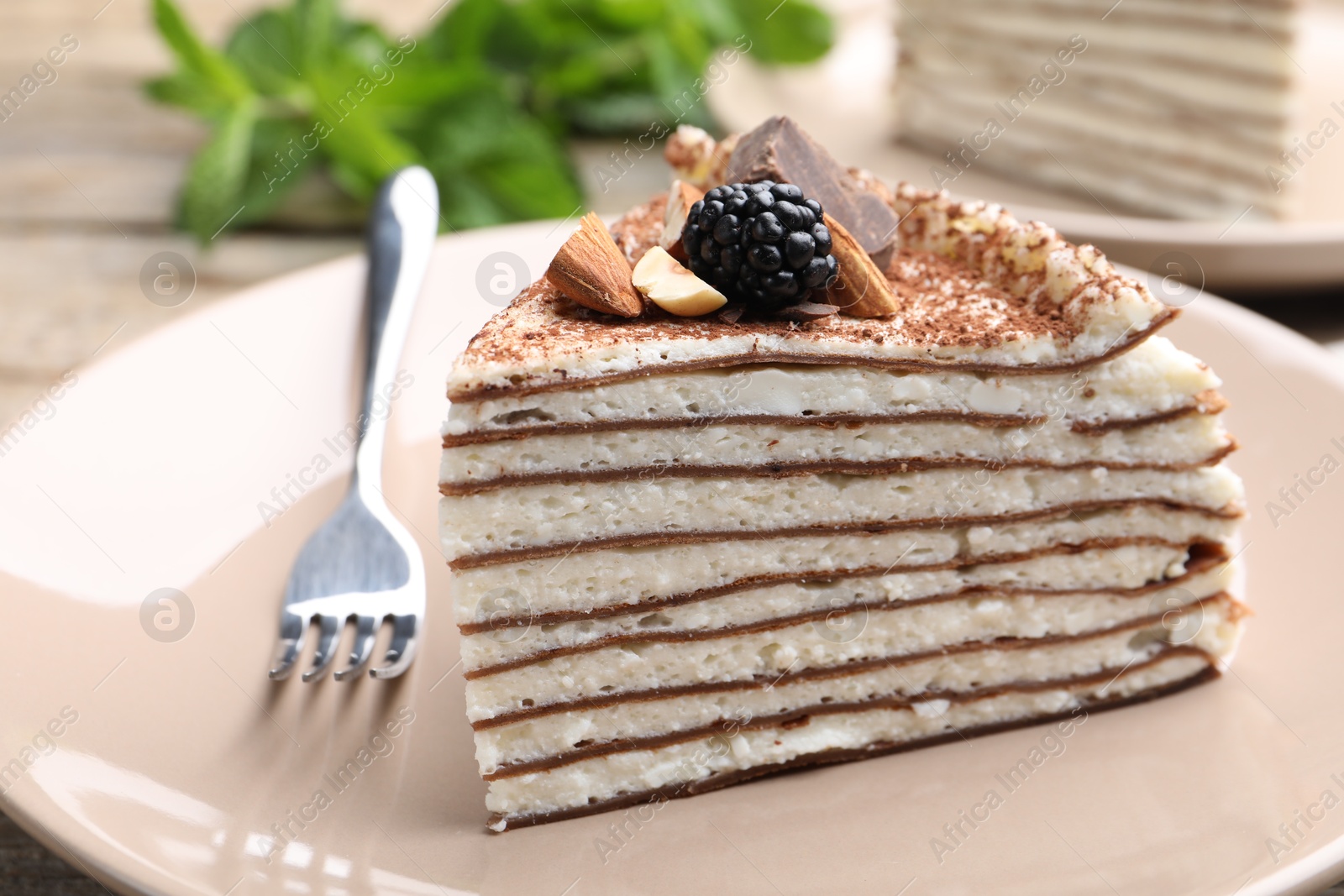 Photo of Piece of tasty crepe cake with cocoa powder, chocolate, nuts and blackberry served on table, closeup