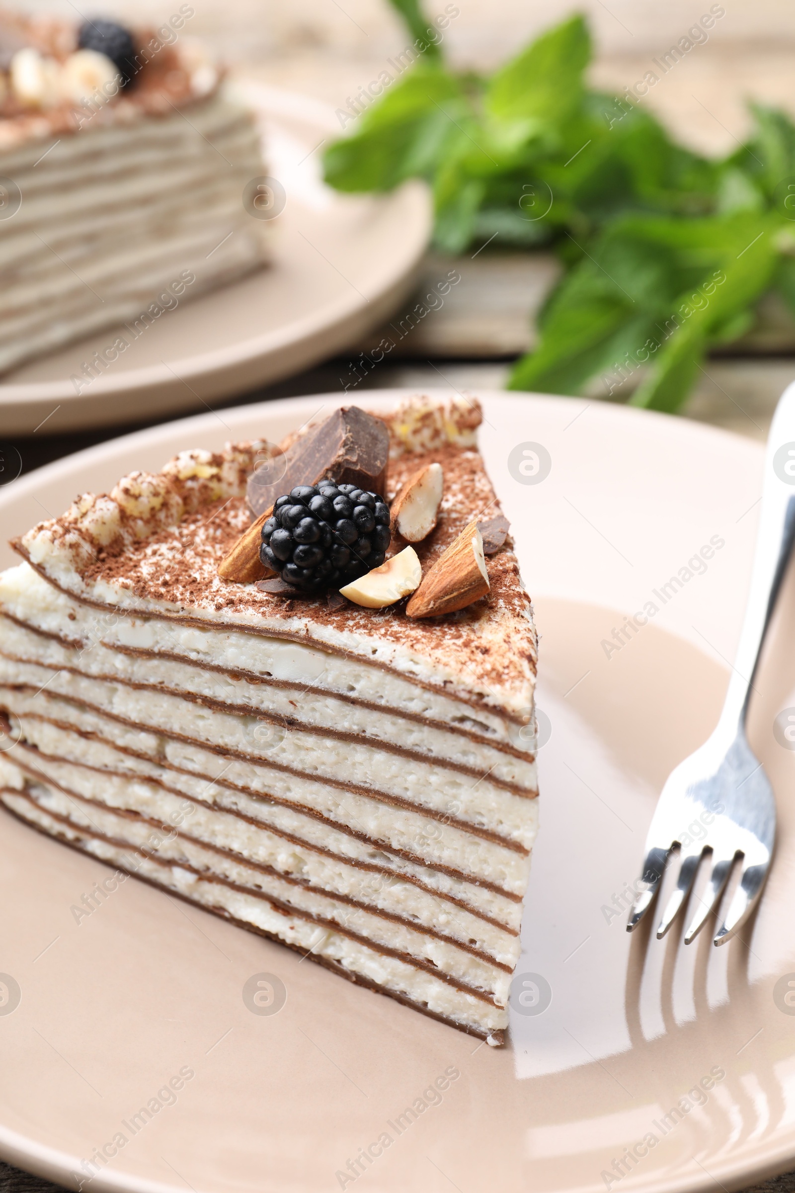 Photo of Piece of tasty crepe cake with cocoa powder, chocolate, nuts and blackberry served on table, closeup