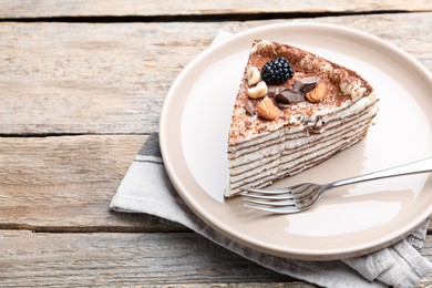 Photo of Piece of tasty crepe cake with cocoa powder, chocolate, nuts and blackberry served on wooden table, closeup. Space for text