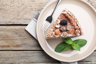 Photo of Piece of tasty crepe cake with cocoa powder, chocolate, nuts and blackberry served on wooden table, top view. Space for text
