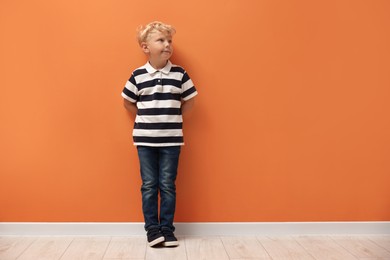 Photo of Cute little boy standing near orange wall