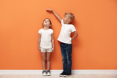 Photo of Cute little girl and boy measuring their heights near orange wall