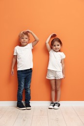 Photo of Cute little girl and boy measuring their heights near orange wall