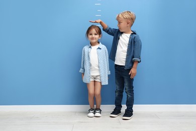 Photo of Cute little girl and boy measuring their heights near blue wall