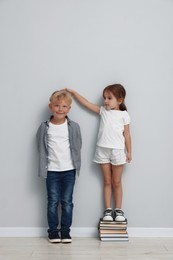 Photo of Cute little girl and boy measuring their heights near light wall