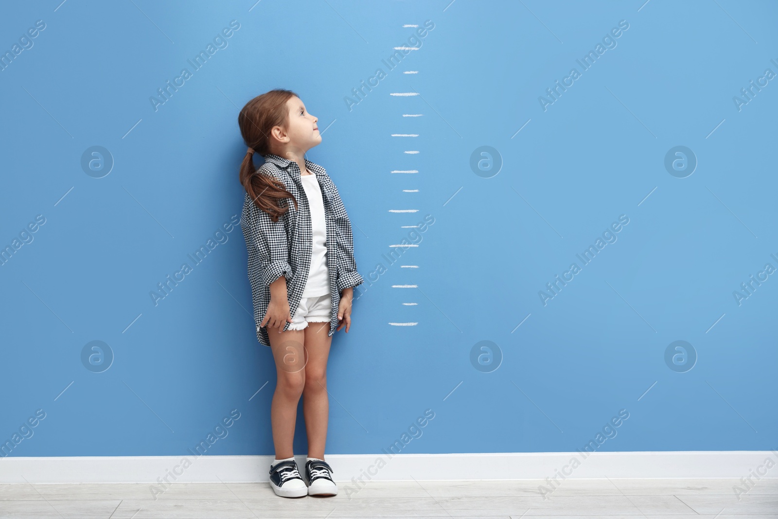 Cute little girl measuring her height near blue wall Photo of Cute little girl measuring her height near blue wall