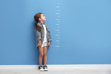Photo of Cute little girl measuring her height near blue wall