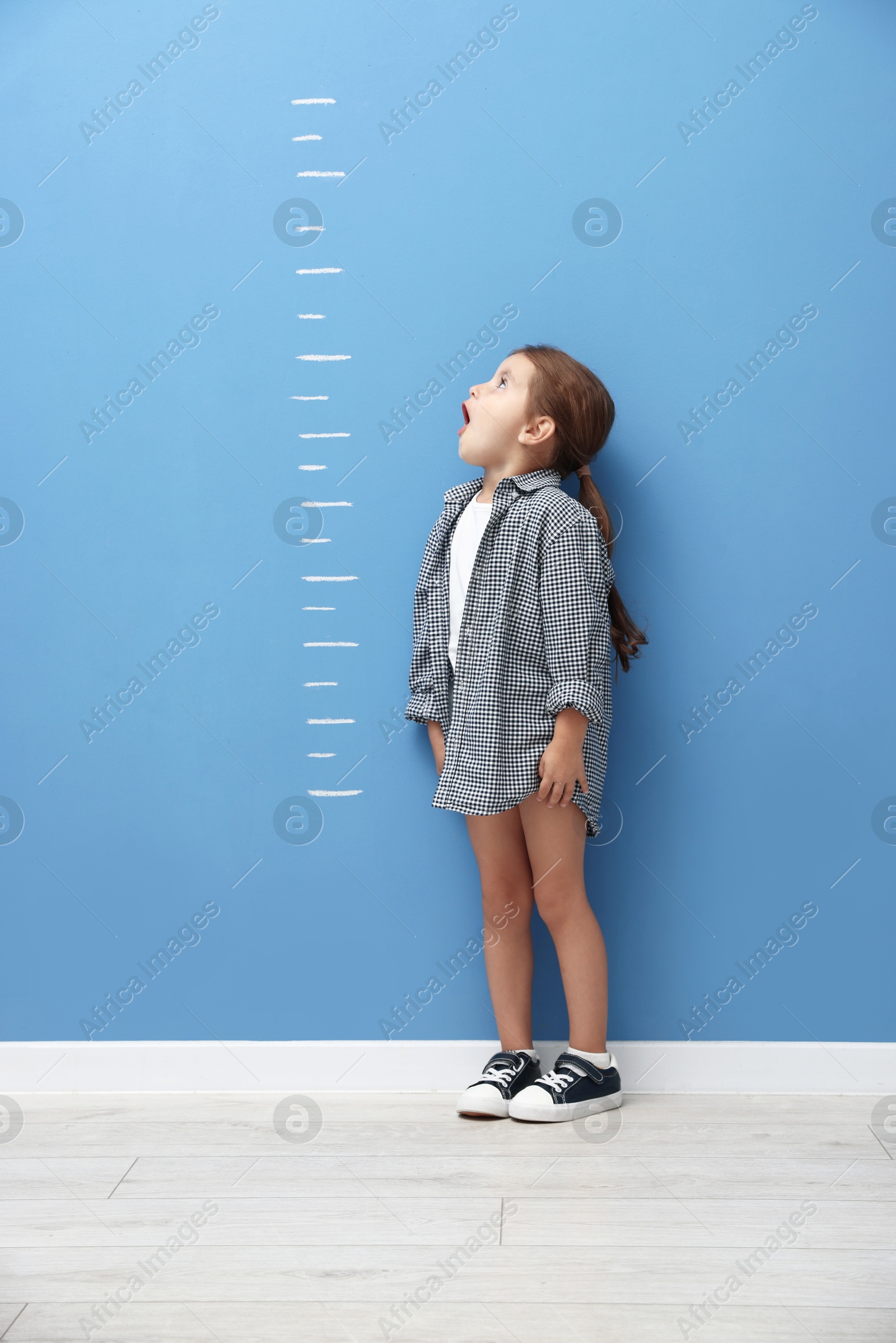Cute little girl measuring her height near blue wall Photo of Cute little girl measuring her height near blue wall