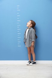 Photo of Cute little girl measuring her height near blue wall