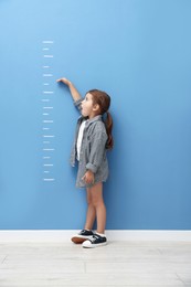 Photo of Cute little girl measuring her height near blue wall