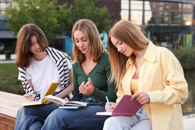 Photo of Teenage girls with notebooks doing homework together outdoors