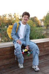Photo of Happy teenage boy with backpack and penny board near lake outdoors