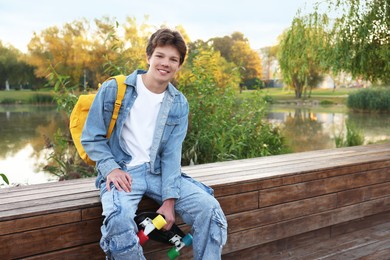 Photo of Happy teenage boy with backpack and penny board near lake outdoors, space for text