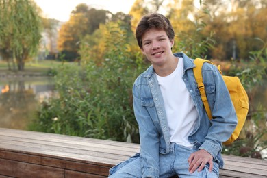 Photo of Happy teenage boy with backpack near lake outdoors, space for text