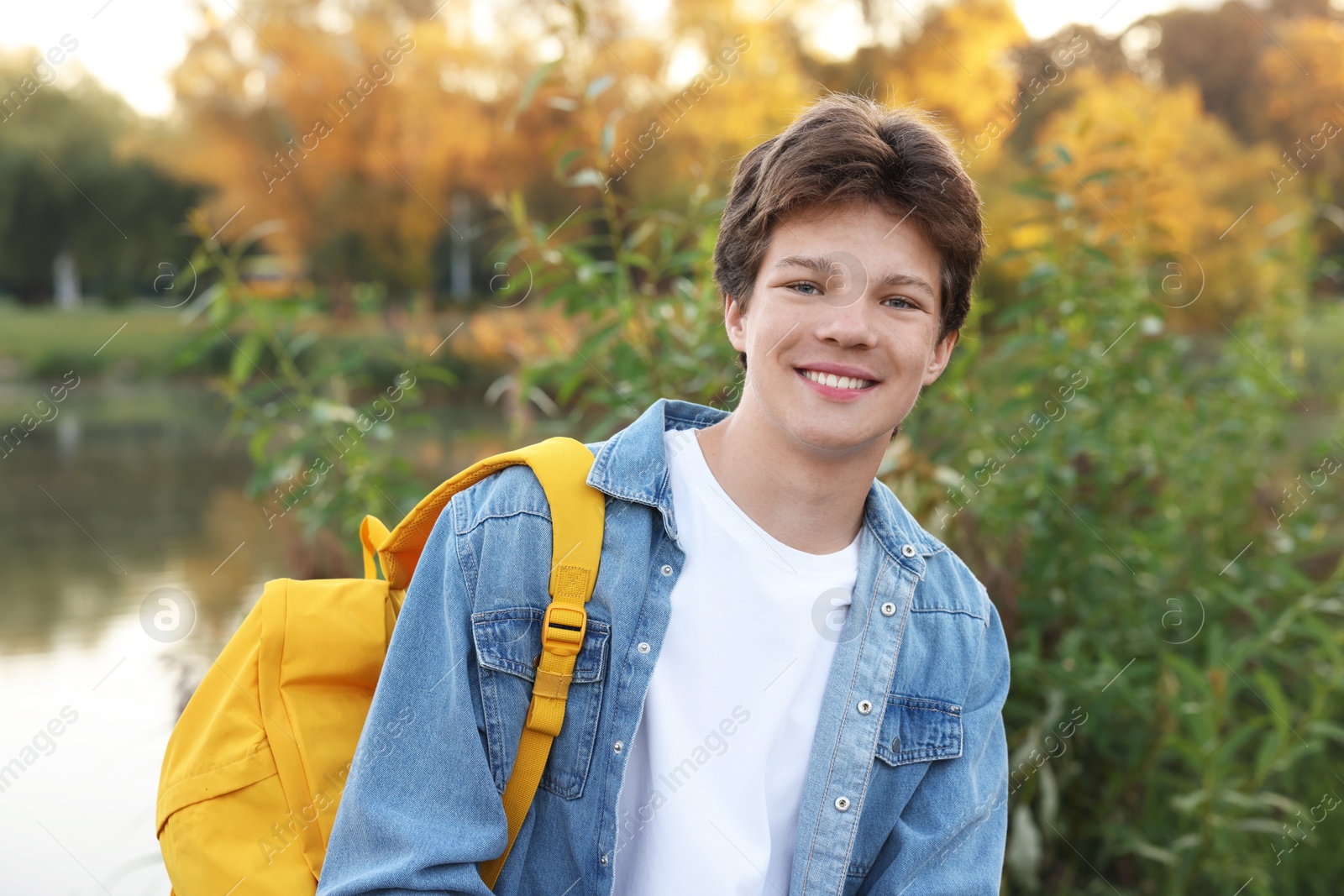 Photo of Happy teenage boy with backpack near lake outdoors
