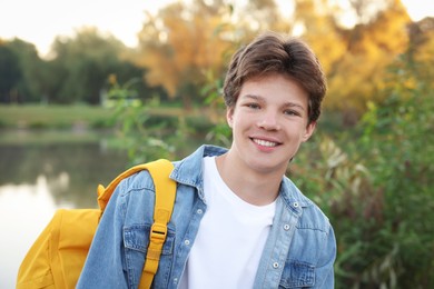 Photo of Happy teenage boy with backpack near lake outdoors