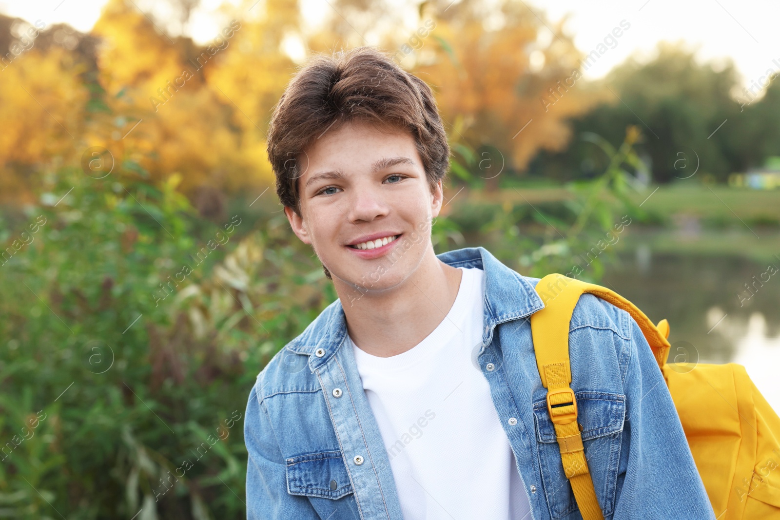 Photo of Happy teenage boy with backpack near lake outdoors