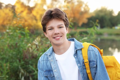 Photo of Happy teenage boy with backpack near lake outdoors