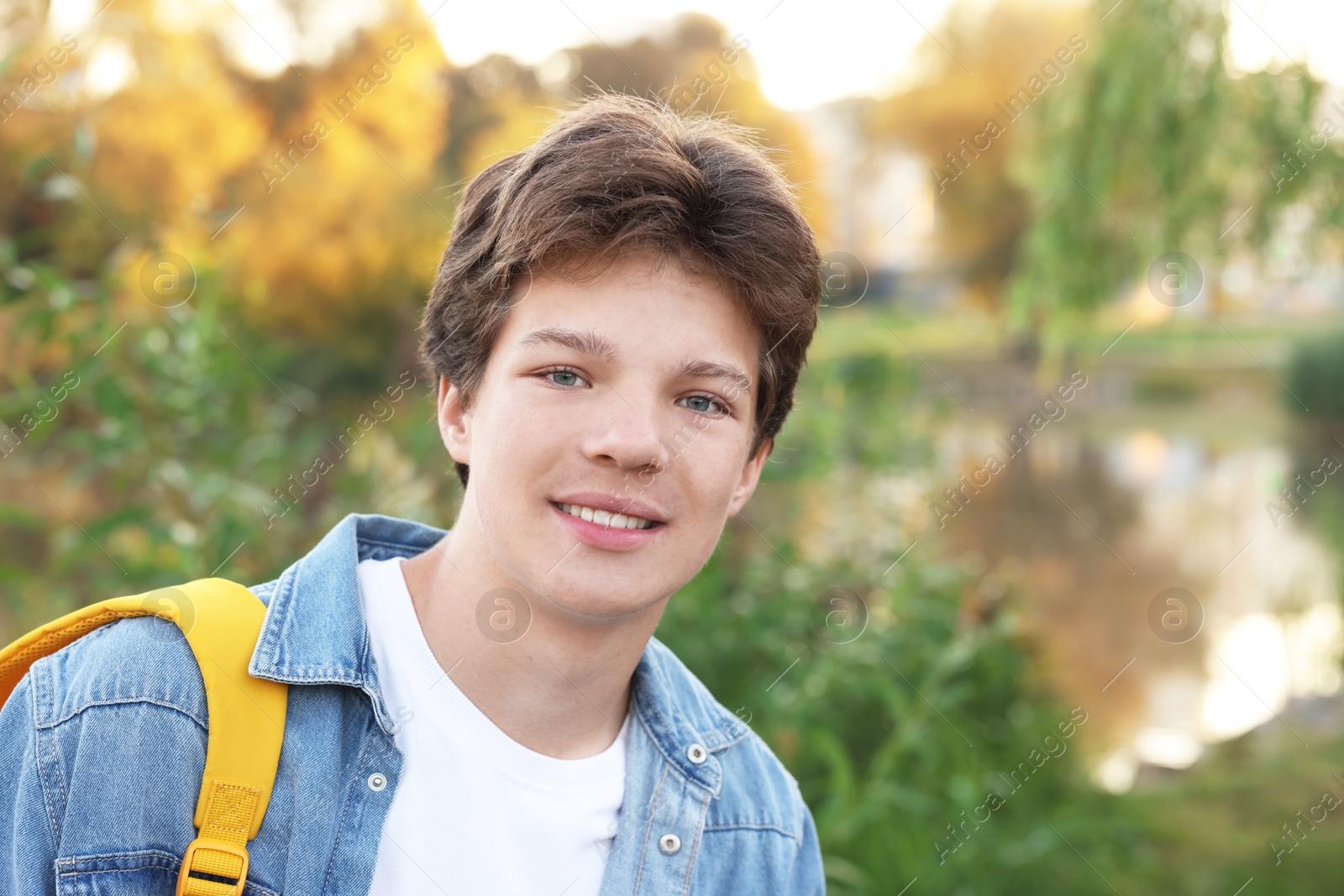 Photo of Happy teenage boy with backpack near lake outdoors, space for text