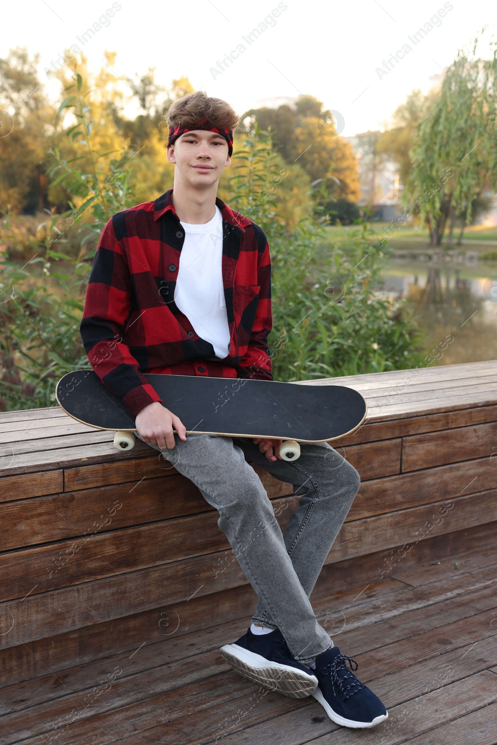 Teenage boy with skateboard on bench near lake outdoors Photo of Teenage boy with skateboard on bench near lake outdoors