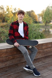Photo of Teenage boy with skateboard on bench near lake outdoors