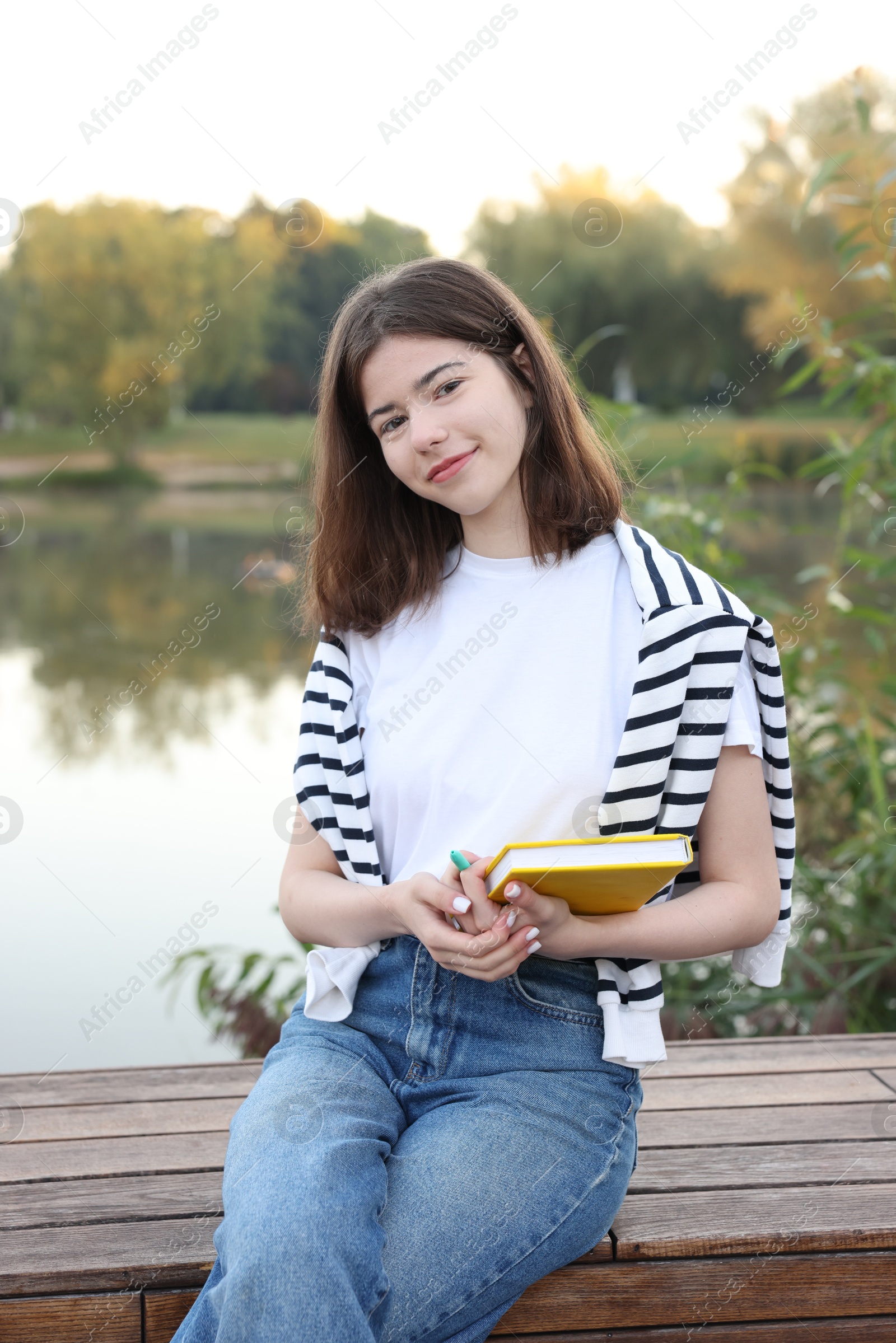 Teenage girl with notebook on bench near lake outdoors Photo of Teenage girl with notebook on bench near lake outdoors