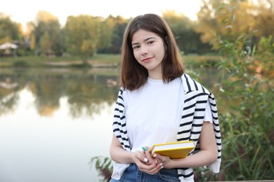 Photo of Teenage girl with notebook near lake outdoors, space for text