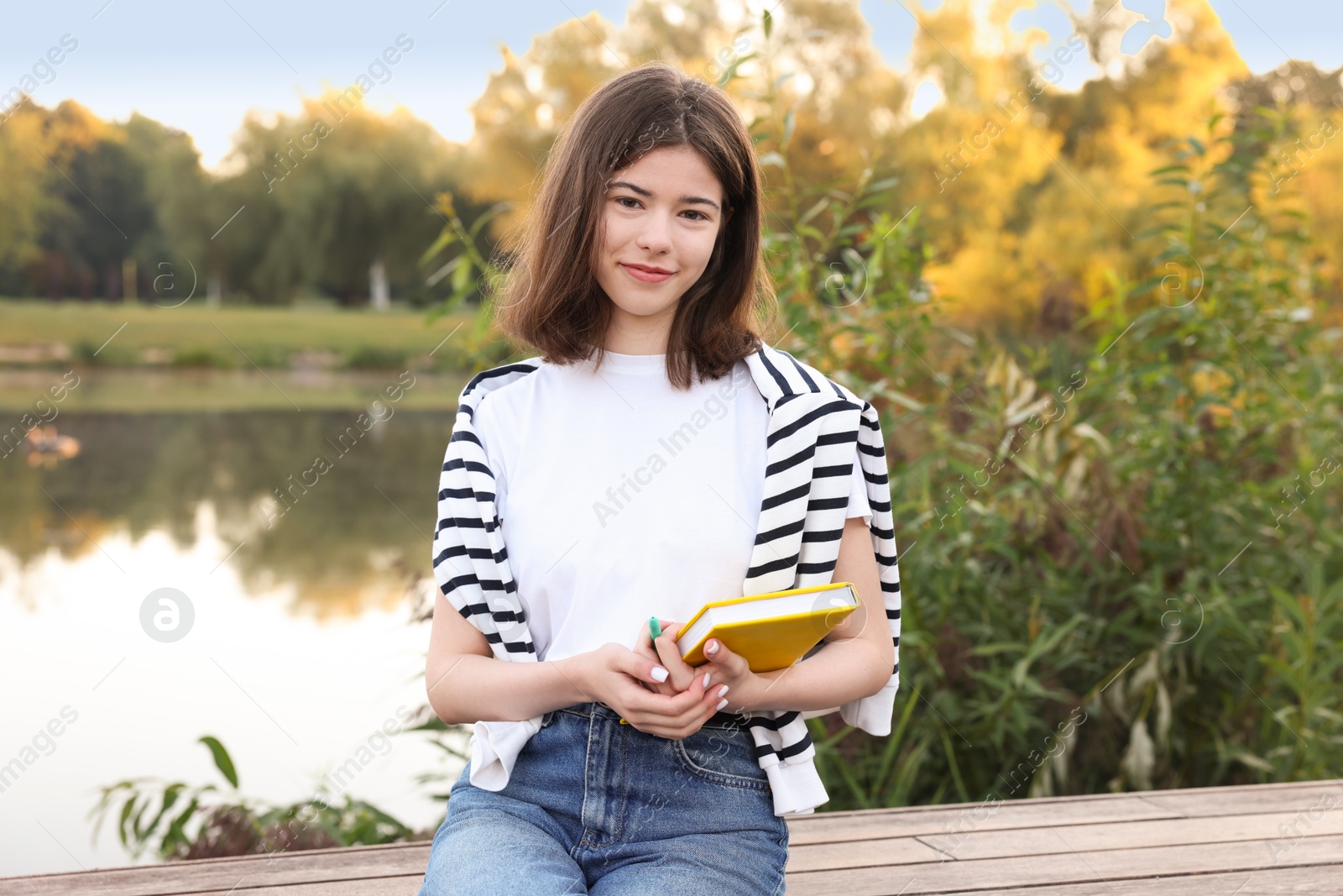 Photo of Teenage girl with notebook on bench near lake outdoors