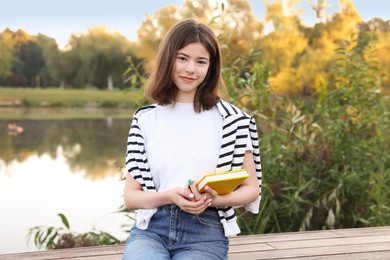 Photo of Teenage girl with notebook on bench near lake outdoors