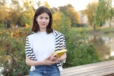 Photo of Teenage girl with notebook on bench near lake outdoors, space for text