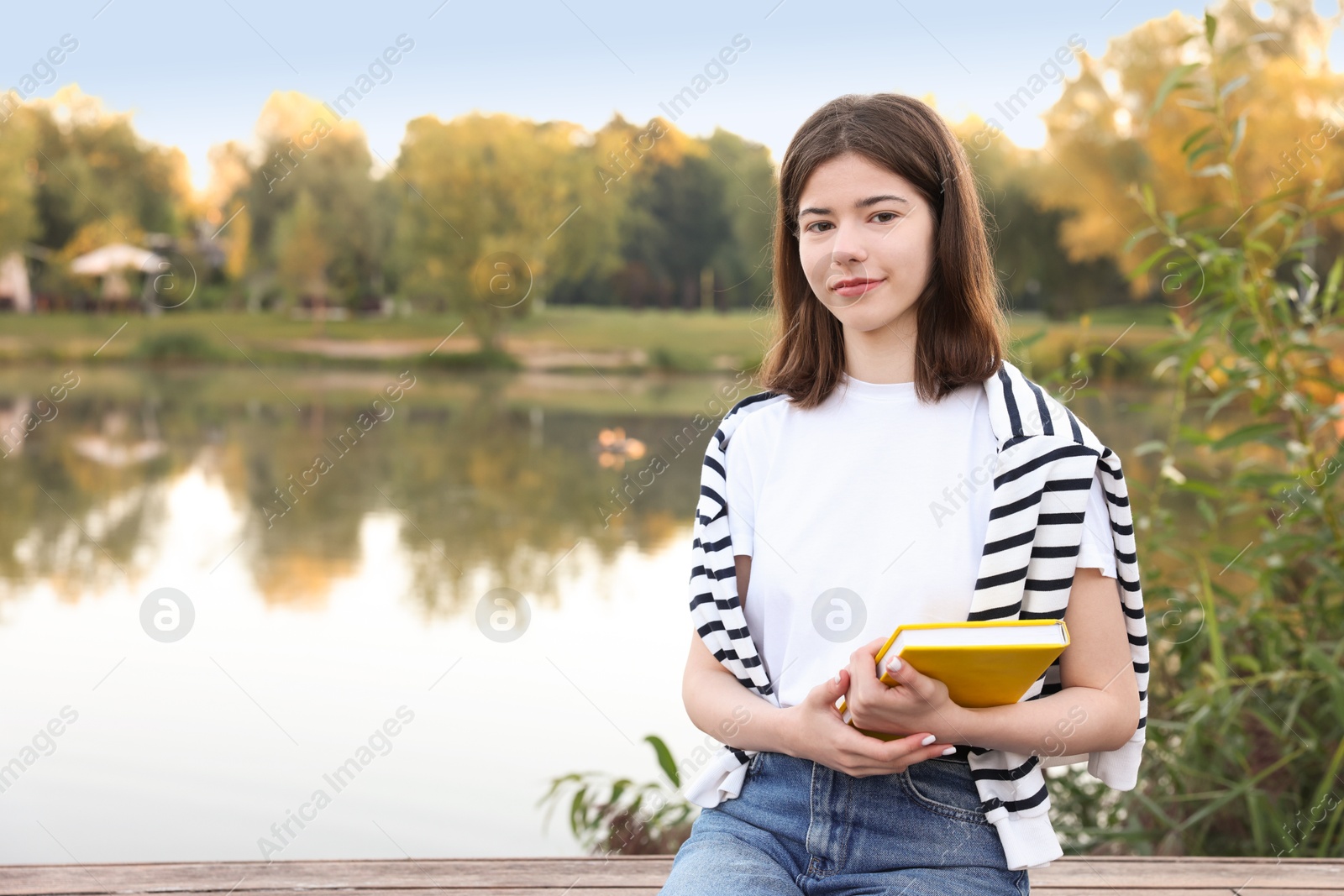 Teenage girl with notebook on bench near lake outdoors, space for text Photo of Teenage girl with notebook on bench near lake outdoors, space for text