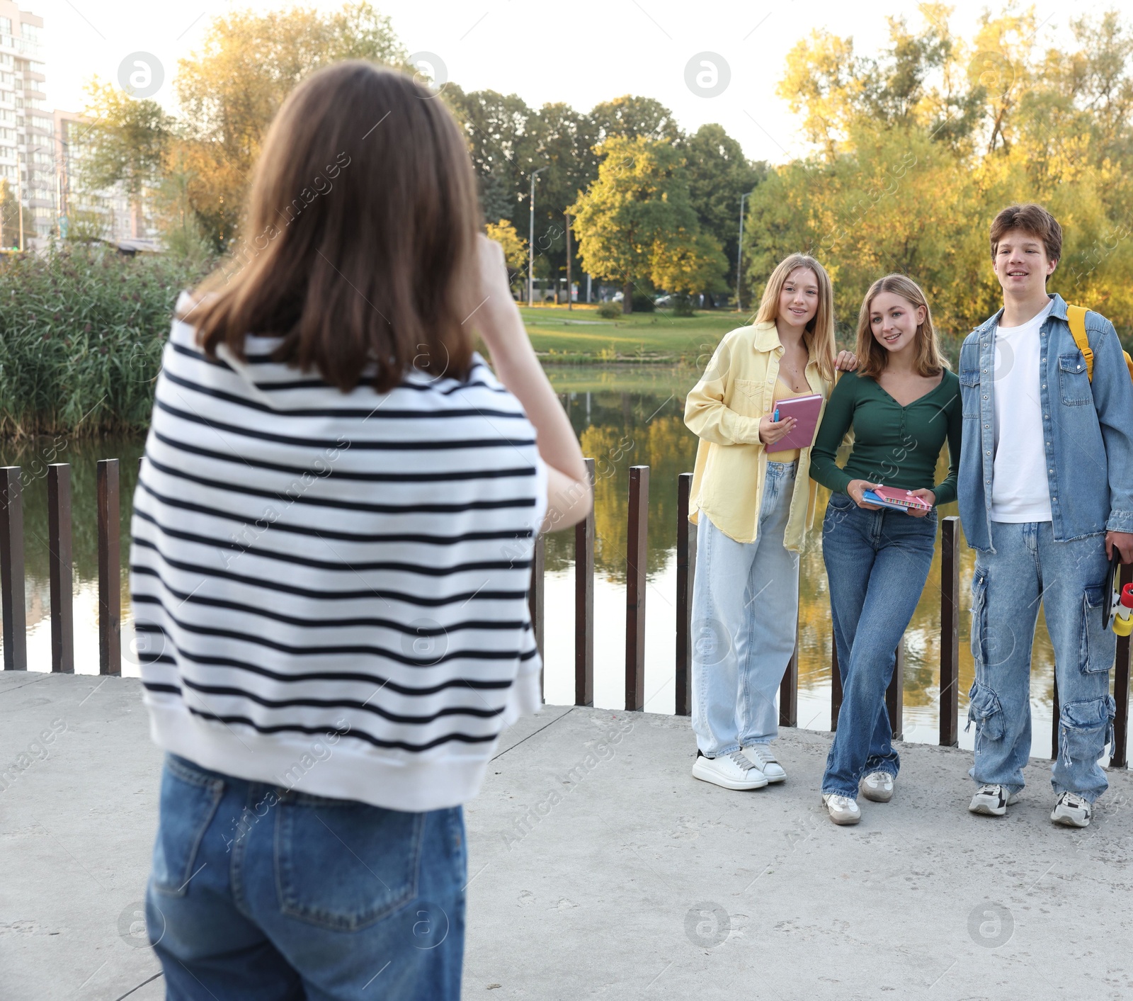 Photo of Teenage girl taking photo of her friends near lake outdoors, back view