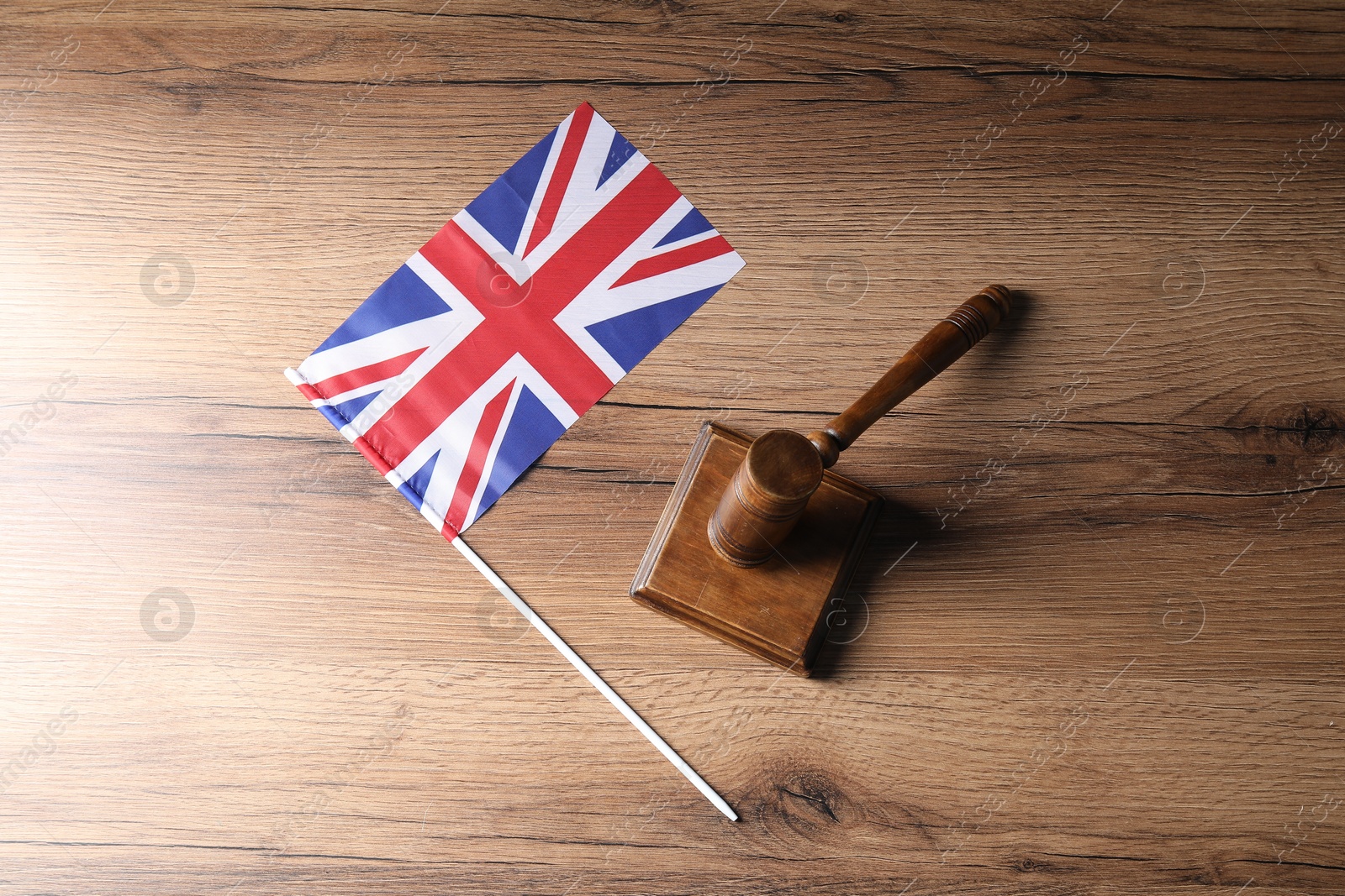 Photo of Judge's gavel and flag of United Kingdom on wooden table, top view
