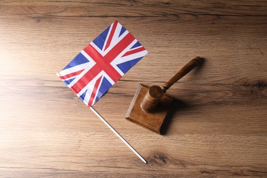 Photo of Judge's gavel and flag of United Kingdom on wooden table, top view