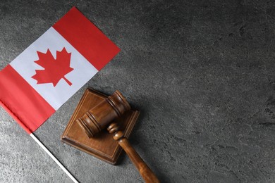 Photo of Judge's gavel and flag of Canada on grey table, top view. Space for text