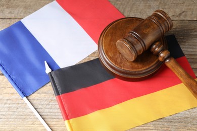 Photo of Judge's gavel and flags of Germany and France on wooden table, closeup