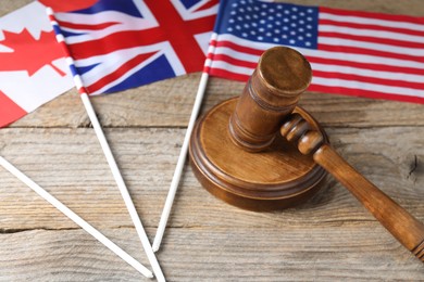 Photo of Judge's gavel and flags of USA, United Kingdom and Canada on wooden table, closeup